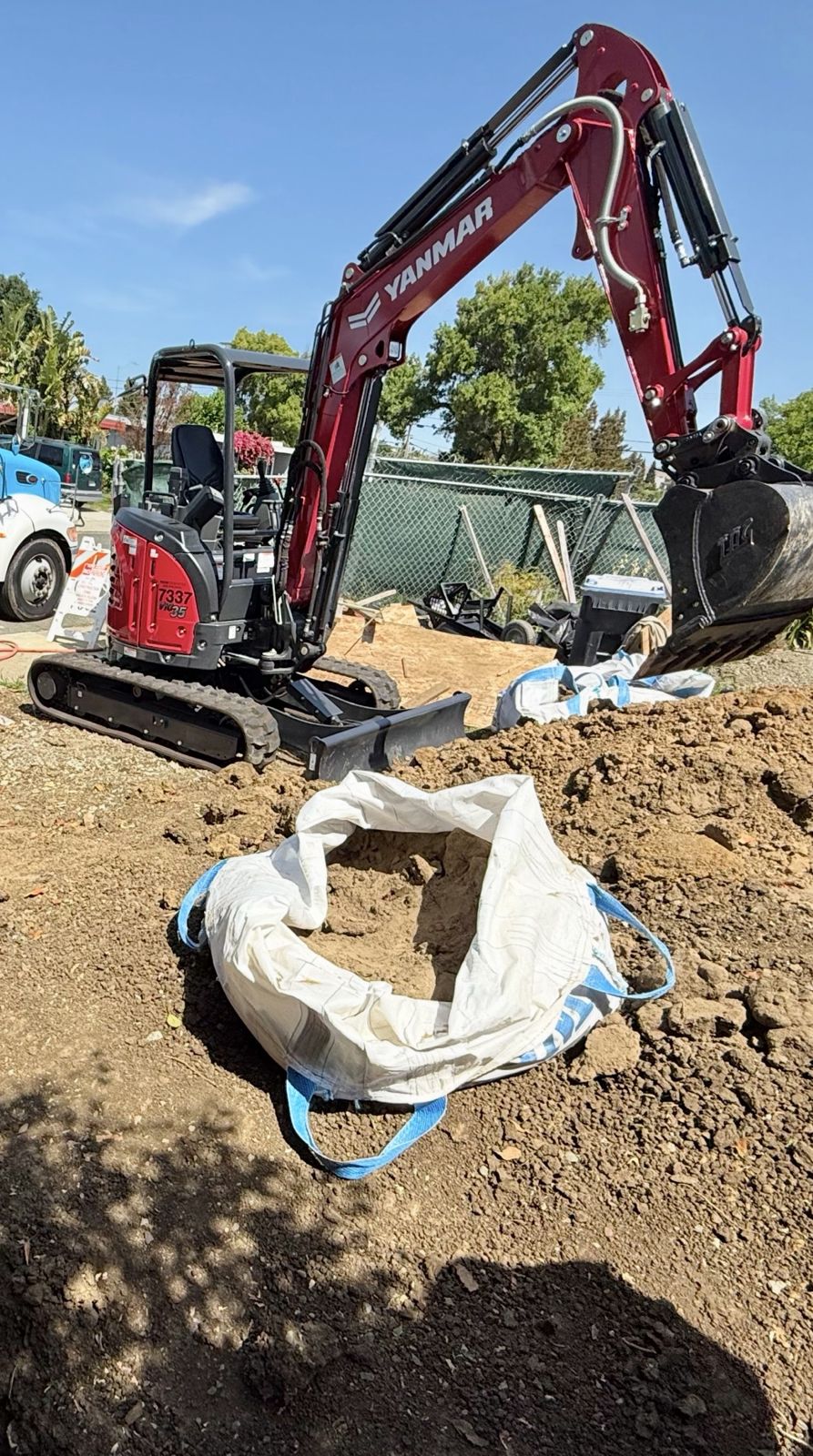 Mini excavator backfilling a utility trench with imported sand