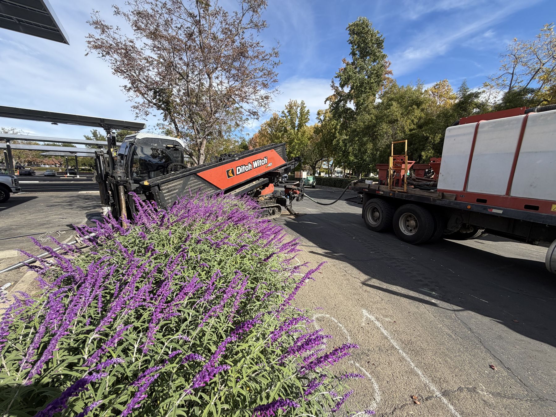 Ditch Witch drill set up in the parking lot next to landscaping and a carport