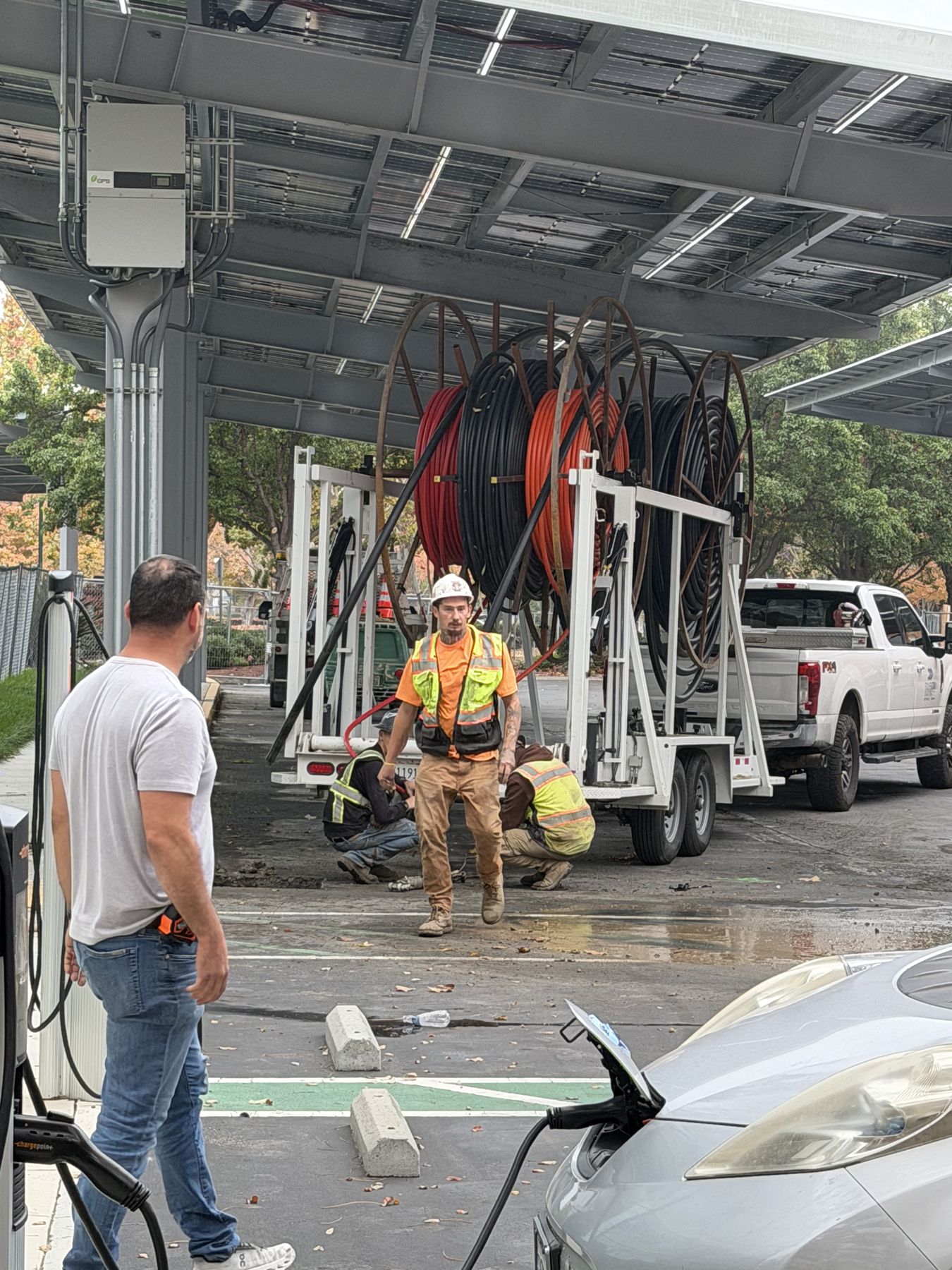 Reel of orange HDPE conduit on a trailer under a solar canopy next to EV chargers