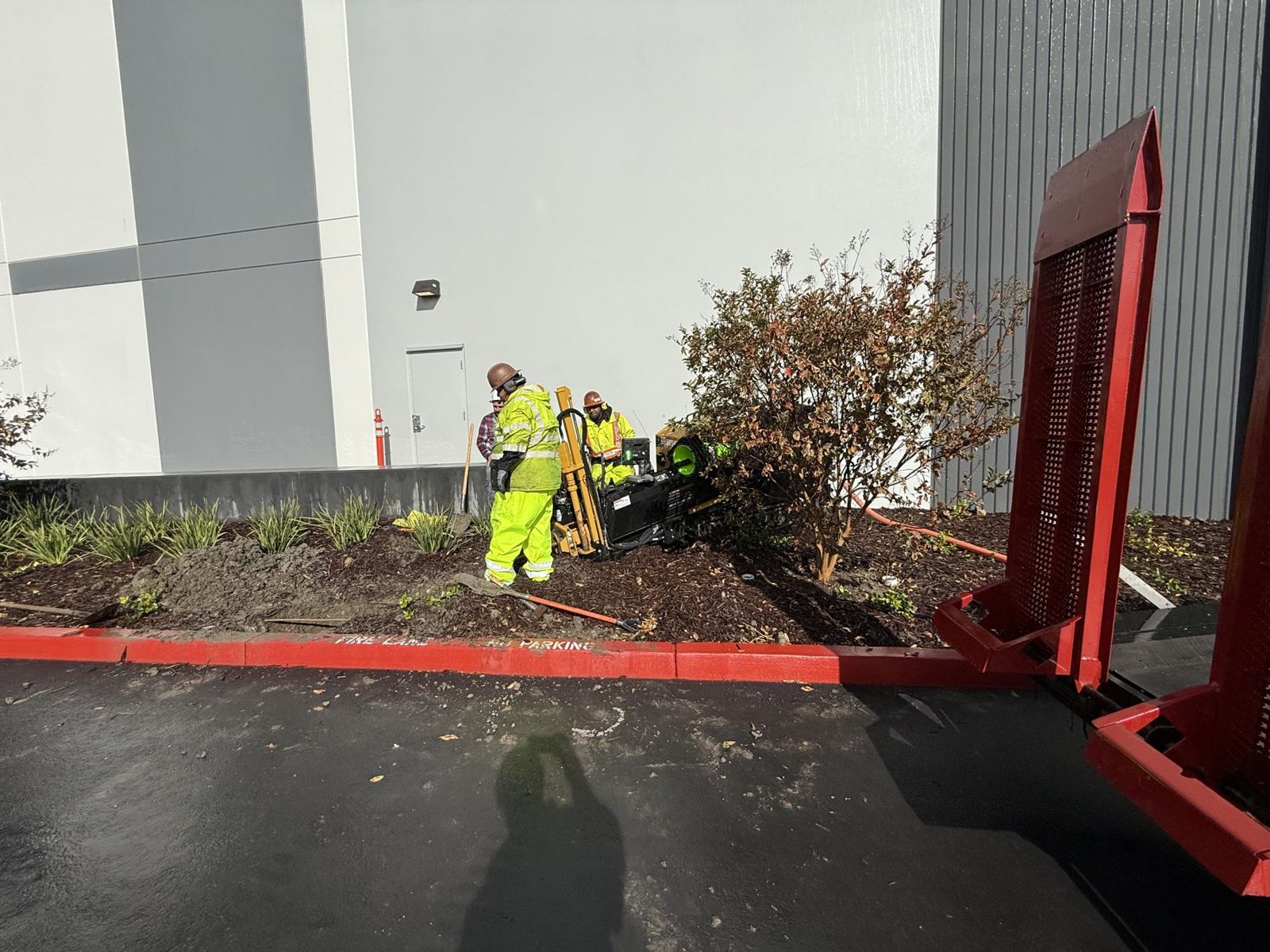Crew working a bore pit in a landscape strip next to a building