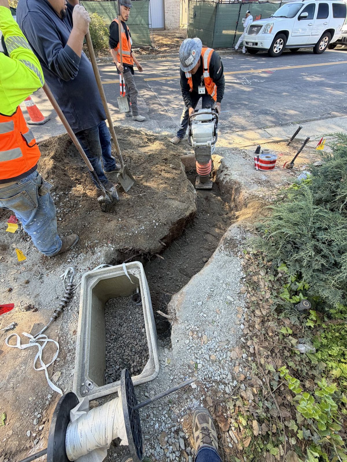 Crew compacting backfill at a pit next to a sidewalk