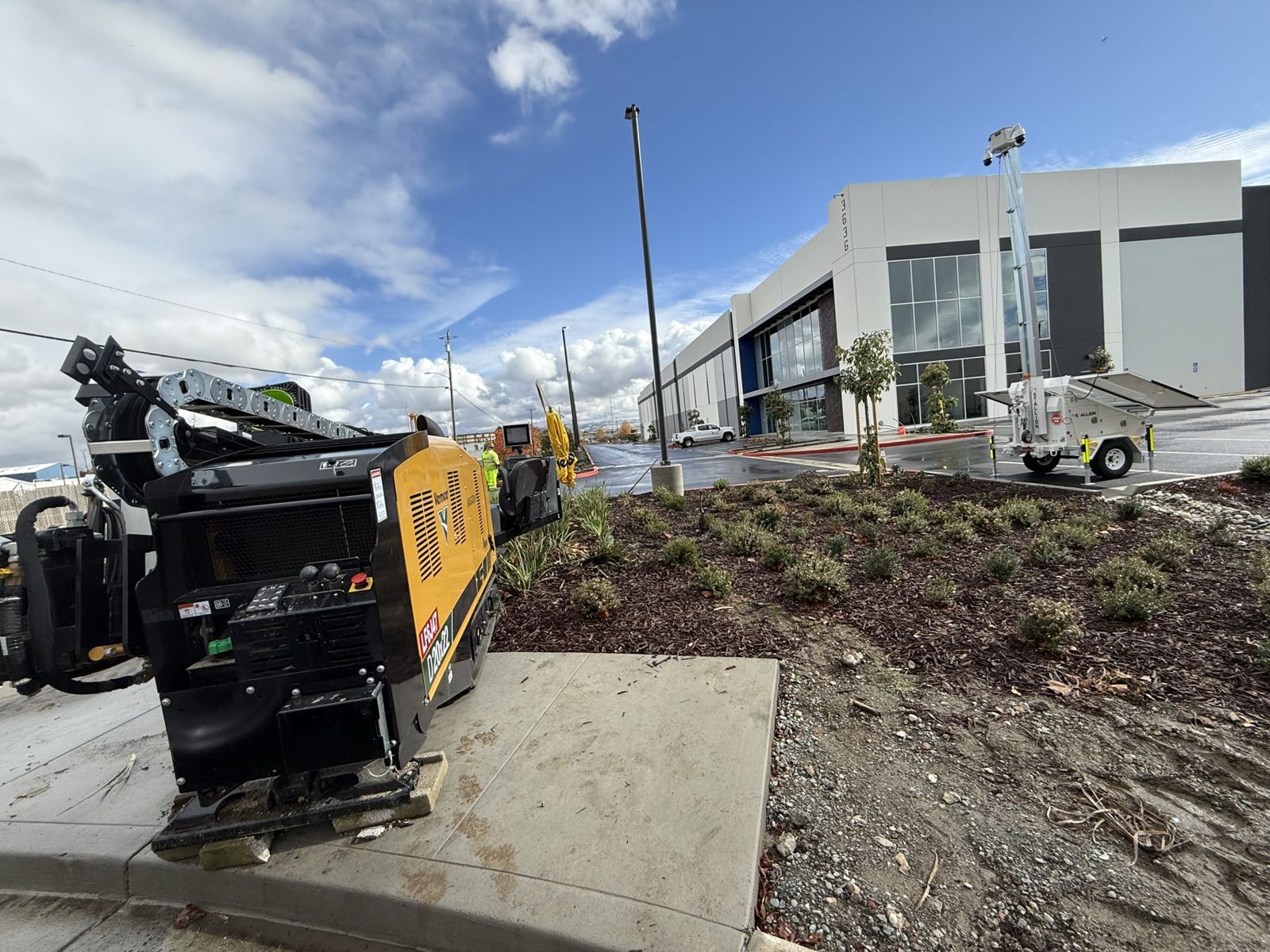 Vermeer D8x12 directional drill set up in a narrow landscape strip beside a commercial building