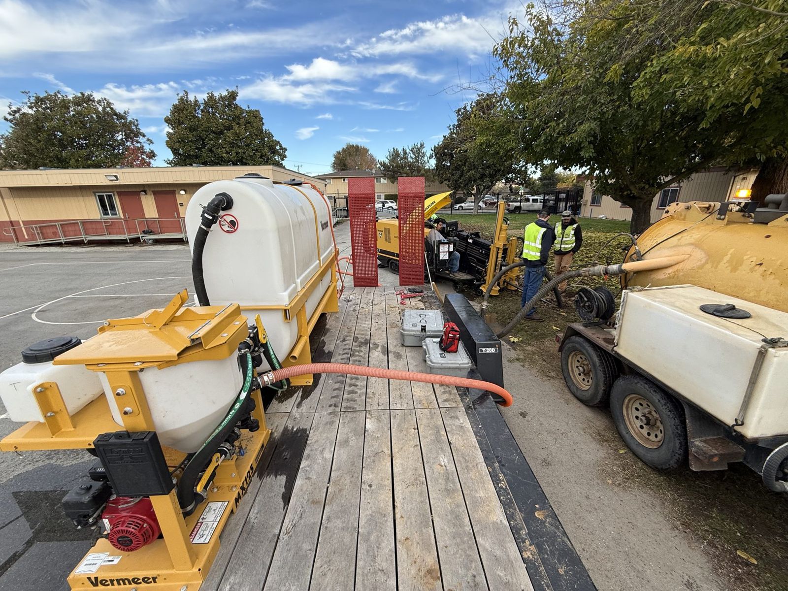 Drill, fluid trailer and vacuum trailer set up on a school yard
